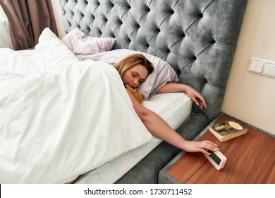 Young Caucasian Woman Pressing Snooze Button On Early Morning Digital Alarm Clock. Selective Focus. Horizontal Shot