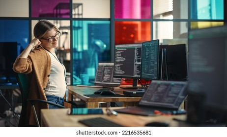 Young Caucasian Woman Programming On Desktop Computer With Two Monitors Setup In Spacious Office. Female Software Developer Creating SaaS Platform, Stretching Before Continuing To Work.