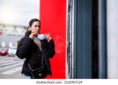 young caucasian woman puts a mask before entering a shop - Shutterstock ID 2132907129