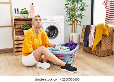 Young Caucasian Woman Putting Dirty Laundry Into Washing Machine Puffing Cheeks With Funny Face. Mouth Inflated With Air, Crazy Expression. 