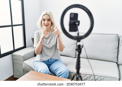 Young Caucasian Woman Recording Vlog Tutorial With Smartphone At Home Pointing Fingers To Camera With Happy And Funny Face. Good Energy And Vibes. 