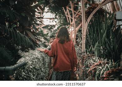 young caucasian woman in red corduroy jacket walking calmly and relaxed on her back inside a botanic garden while caressing the soft leaves of the plants, botanic garden christchurch, new zealand - Shutterstock ID 2311570637