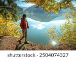 Young Caucasian woman in a red down jacket walking near turquoise lake in mountains.