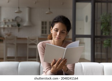 Young Caucasian woman relax on couch at cozy home read interesting book. Happy millennial female renter or tenant rest on sofa in living room enjoy novel or story on weekend. Hobby concept.