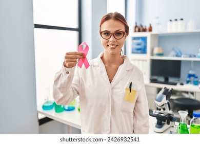 Young caucasian woman scientist smiling confident holding pink cancer ribbon at laboratory - Powered by Shutterstock