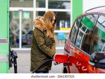 Young caucasian woman at self-service gas station, hold fuel nozzle and refuel the car with petrol, diesel, gas. Pretty woman filling her auto with gasoline or benzine, outdoors. Self service gas pump