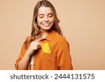 Young Caucasian woman she wear orange shirt casual clothes hold in hand put mock up of credit bank card into pocket isolated on plain pastel light beige background studio portrait. Lifestyle concept