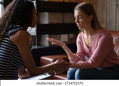 Young Caucasian woman sit on couch in coffee house talking with  psychologist telling problems, stressed female meeting with African American coach or marriage counselor speaking in cafe