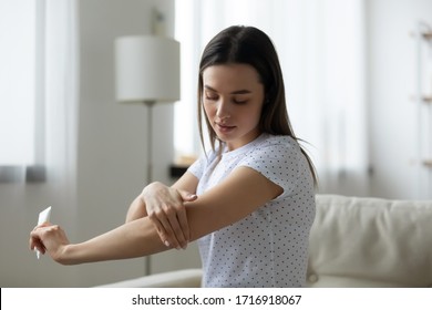 Young Caucasian Woman Sit On Couch In Living Room Using Moisturizing Body Cream For Soft Healthy Skin, Millennial Girl Relax At Home Do Daily Beauty Spa Procedures, Apply Nourishing Balm On Arms Hands