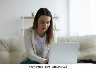 Young Caucasian Woman Sit On Couch At Home Look At Laptop Screen Surfing Web Texting Messaging Online. Millennial Female Busy Using Modern Computer Gadget, Browse Wireless Internet On Device.