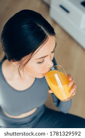 Young Caucasian woman sitting on the floor and drinking orange juice from the glass - Shutterstock ID 1781329592