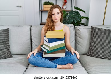 Young caucasian woman sitting on the sofa with books at home depressed and worry for distress, crying angry and afraid. sad expression. 