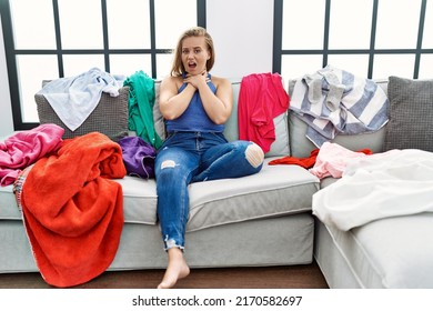 Young caucasian woman sitting on the sofa at home around dirty laundry shouting and suffocate because painful strangle. health problem. asphyxiate and suicide concept. 