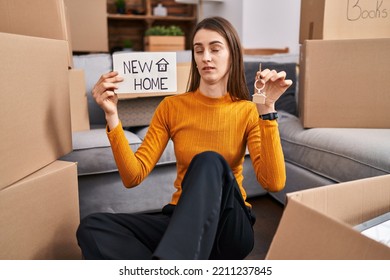 Young Caucasian Woman Sitting On The Floor At New Home Holding New Home Banner Clueless And Confused Expression. Doubt Concept. 