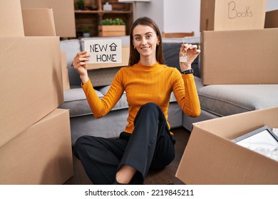 Young Caucasian Woman Sitting On The Floor At New Home Holding New Home Banner Smiling With A Happy And Cool Smile On Face. Showing Teeth. 