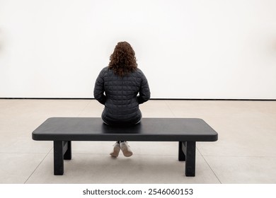 Young Caucasian Woman Sitting on a Bench in a Minimalist Room, Contemplating - Powered by Shutterstock