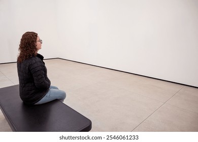 Young Caucasian Woman Sitting on a Bench in a Minimalist Room, Contemplating - Powered by Shutterstock