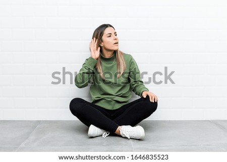 Young caucasian woman sitting on the floor trying to listening a gossip.