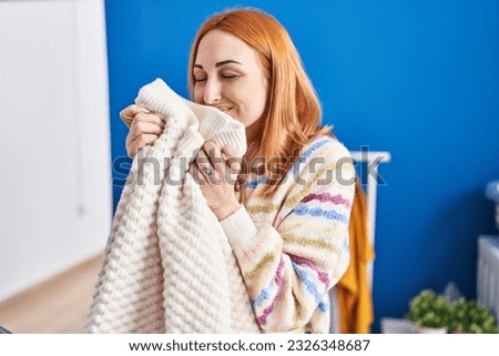 Young caucasian woman smelling sweater standing at laundry room