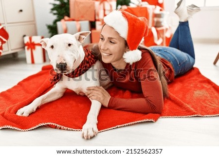 Young caucasian woman smiling confident hugging dog lying by christmas tree at home
