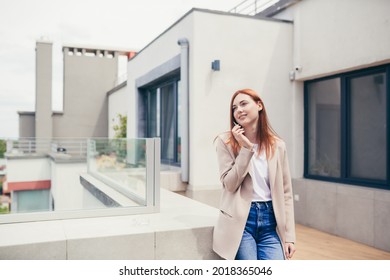 Young Caucasian Woman Standing On The Terrace Of A Modern Office Or Balcony At Home And Smokes Marijuana. Business Lady Smoking Cannabis. Female Relieves Stress At Work A Light Drug. Businesswoman