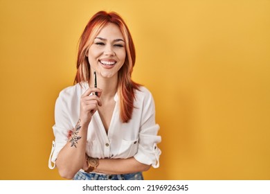 Young Caucasian Woman Standing Over Yellow Background Holding Pen Smiling And Laughing Hard Out Loud Because Funny Crazy Joke. 