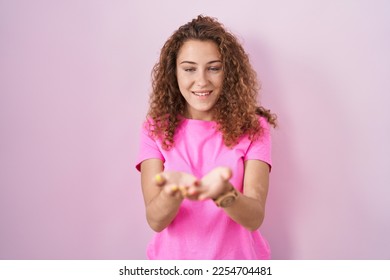 Young caucasian woman standing over pink background smiling with hands palms together receiving or giving gesture. hold and protection  - Shutterstock ID 2254704481