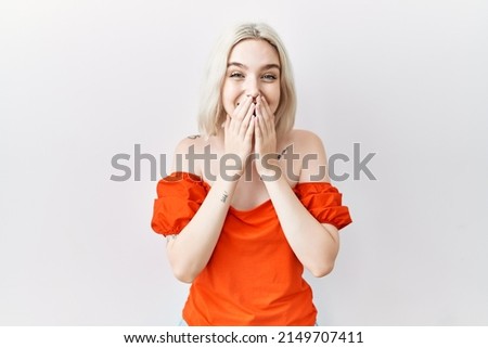 Young caucasian woman standing over isolated background laughing and embarrassed giggle covering mouth with hands, gossip and scandal concept 