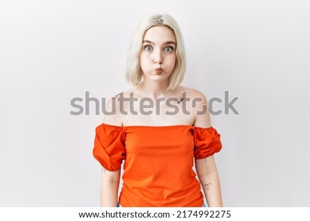 Young caucasian woman standing over isolated background puffing cheeks with funny face. mouth inflated with air, crazy expression. 