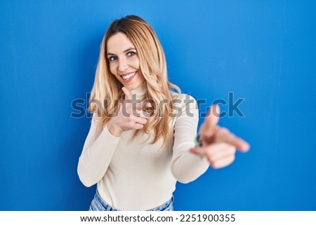 Young caucasian woman standing over blue background pointing fingers to camera with happy and funny face. good energy and vibes. 