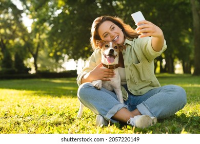 Young caucasian woman student female pet owner taking selfie photo image on smart phone, having video call conversation with dog jack russell terrier online in park