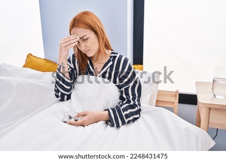 Young caucasian woman taking pills for headache sitting on bed at bedroom