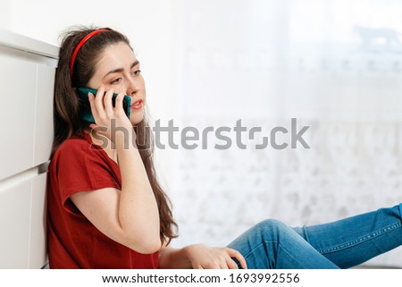A young Caucasian woman is talking on a helpline. White window in the background. Copy space. Concept of modern technologies and social assistance