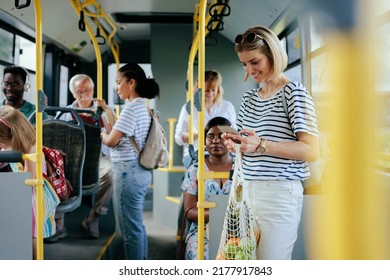 A young caucasian woman is texting on her smartphone in a city bus after shopping for groceries