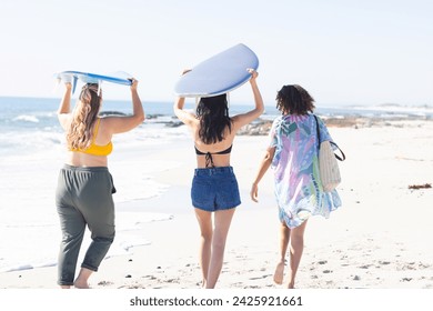 Young Caucasian woman and two young biracial women enjoy the beach. They carry surfboards, ready for a day of surfing in the outdoor setting. - Powered by Shutterstock