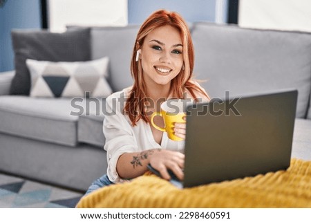 Young caucasian woman using laptop and earphones drinking coffee at home
