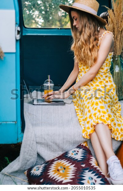 Young caucasian woman using laptop computer\
while sitting o a van\
outdoors.