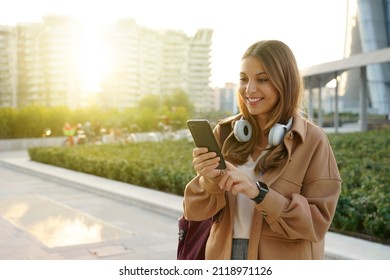 Young caucasian woman using a phone on modern city background at sunset - Powered by Shutterstock