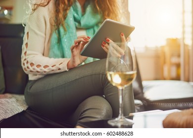 Young Caucasian Woman Using Tablet In Living Room While Drinking Wine