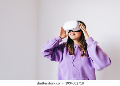 Young caucasian woman using VR headset, touching glasses and looking up in virtual reality on gray background. - Powered by Shutterstock