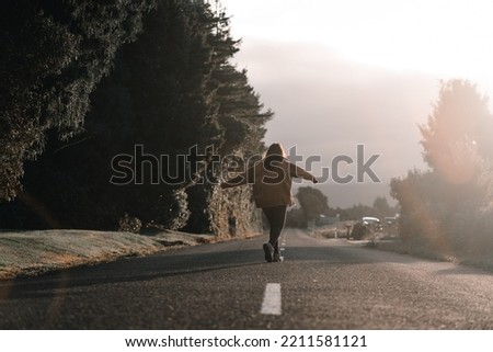 young caucasian woman walking backwards happy and calm with arms outstretched along a quiet long narrow road with no traffic enjoying freedom
