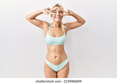 Young caucasian woman wearing bikini over isolated background doing peace symbol with fingers over face, smiling cheerful showing victory 