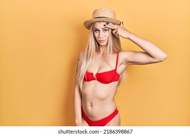 Young caucasian woman wearing bikini and summer hat pointing unhappy to pimple on forehead, ugly infection of blackhead. acne and skin problem 