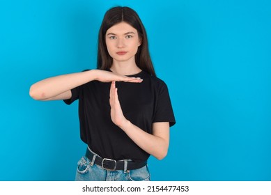 Young caucasian woman wearing black T-shirt over blue background feels tired and bored, making a timeout gesture, needs to stop because of work stress, time concept.