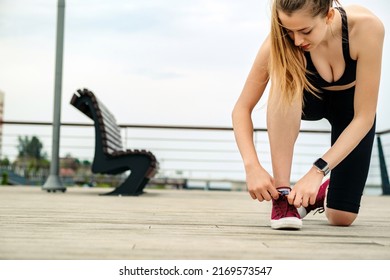 Young caucasian woman wearing black sports bra standing on city park, outdoors tying lace running shoes getting ready for run. Jogging girl exercise motivation health and fitness.