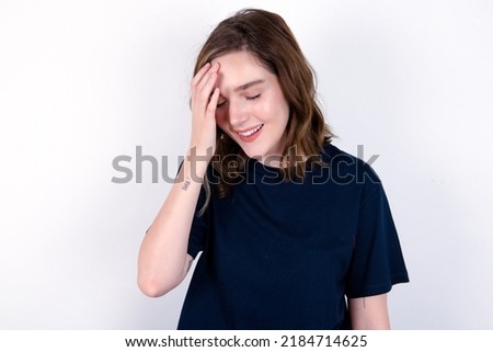 young caucasian woman wearing black T-shirt over white background makes face palm and smiles broadly, giggles positively hears funny joke poses