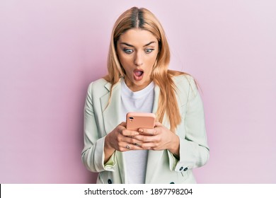 Young caucasian woman wearing business clothes using smartphone afraid and shocked with surprise and amazed expression, fear and excited face. 