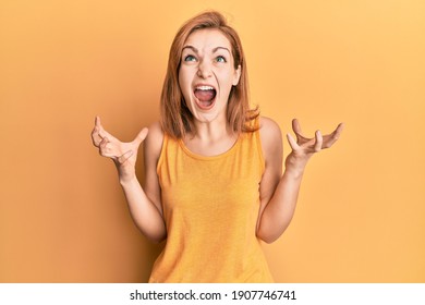 Young caucasian woman wearing casual style with sleeveless shirt crazy and mad shouting and yelling with aggressive expression and arms raised. frustration concept. 