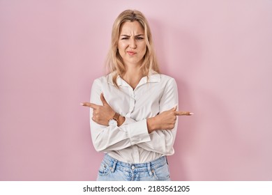 Young caucasian woman wearing casual white shirt over pink background pointing to both sides with fingers, different direction disagree 