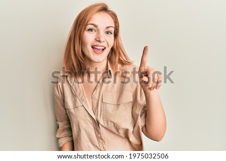 Young caucasian woman wearing casual clothes smiling with an idea or question pointing finger up with happy face, number one 